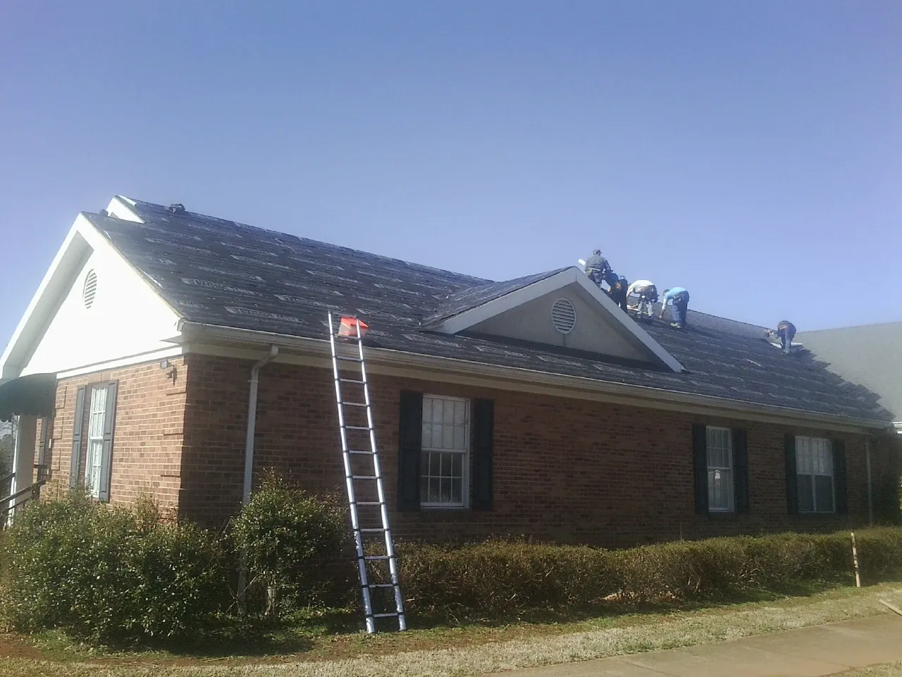 Crew tearing shingles off a brick ranch roof with a ladder set — Emergency Roof Repair work by our crew in Mason City