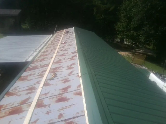 Old rusted panels beside newly installed green metal roofing — Wind Damage Roof Repair by Roofing Brothers in Mason City