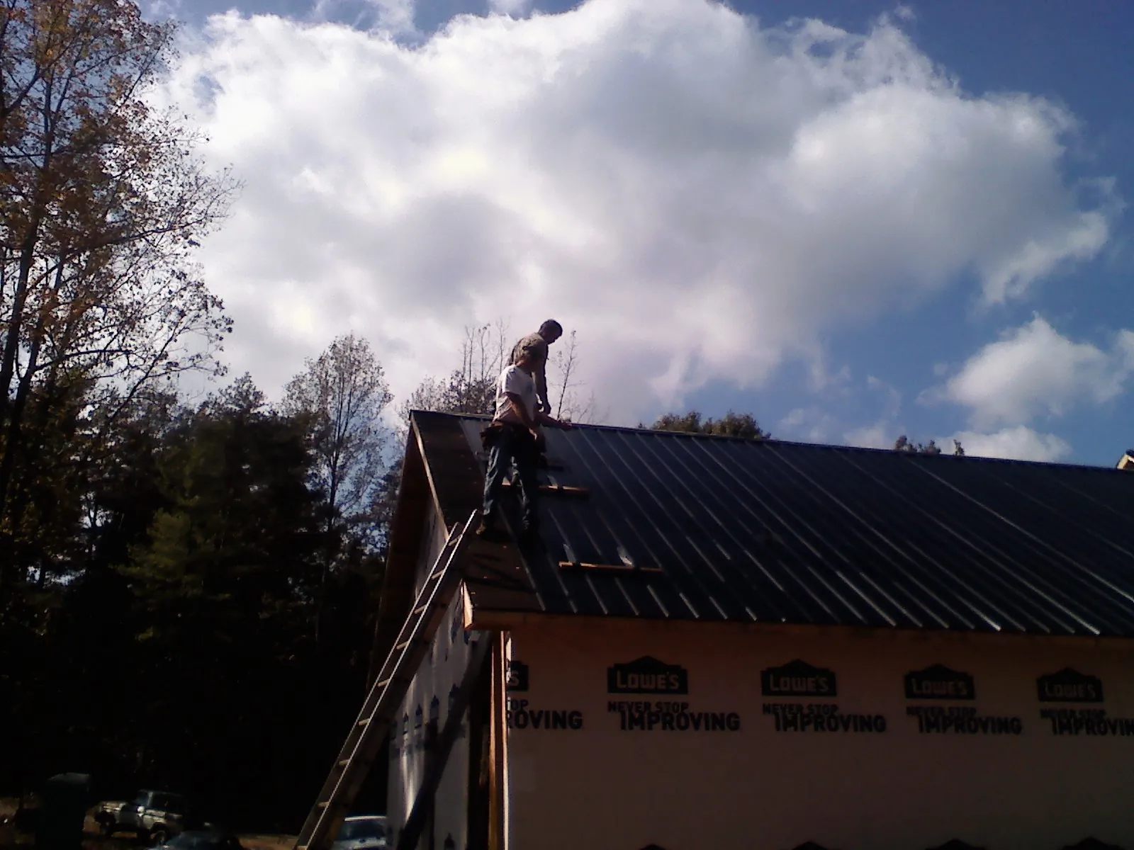 Roofer fastening dark metal panels high against a cloudy sky, from a Roof Inspection job in Mason City