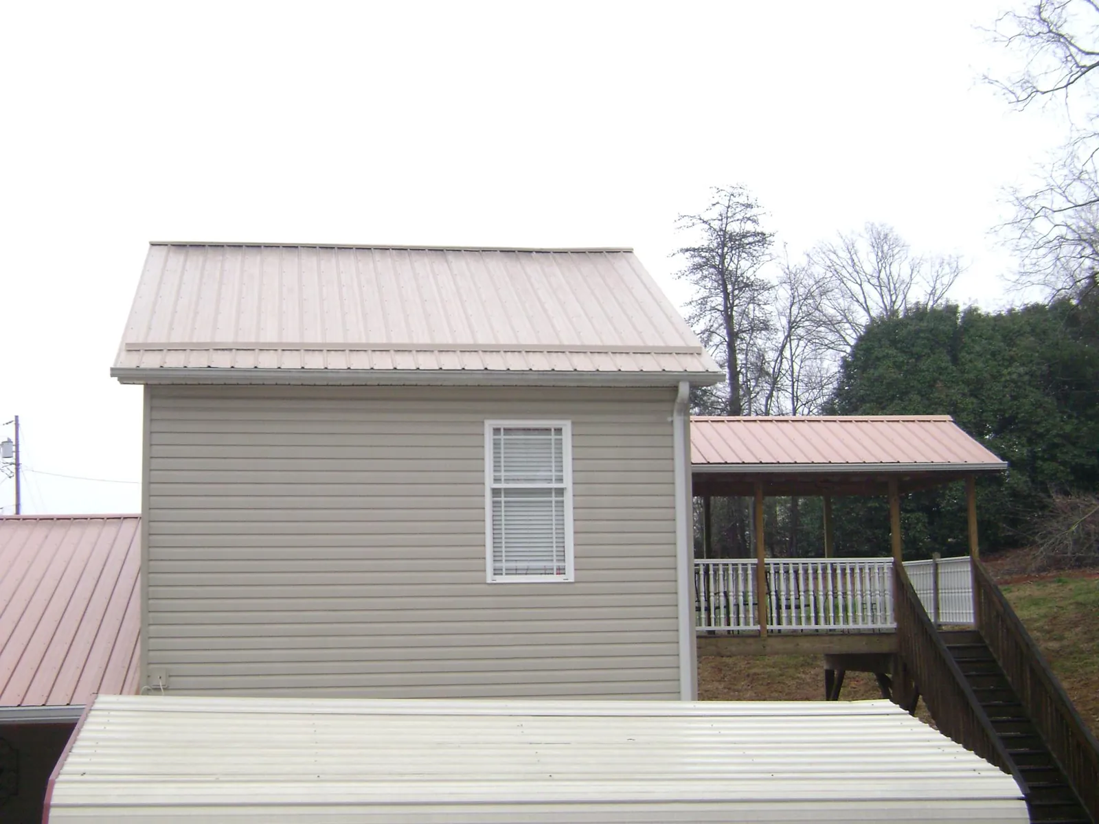 Tan metal roofs on a two story addition and attached porch, from a Roof Replacement job in Mason City